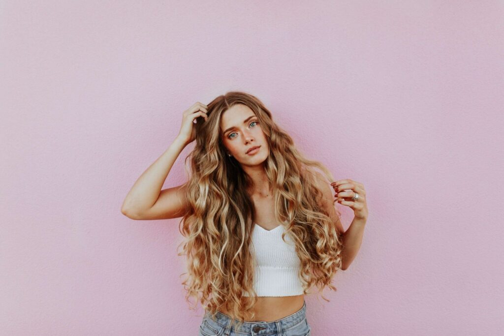 Blonde woman with long hair in front of pink wall