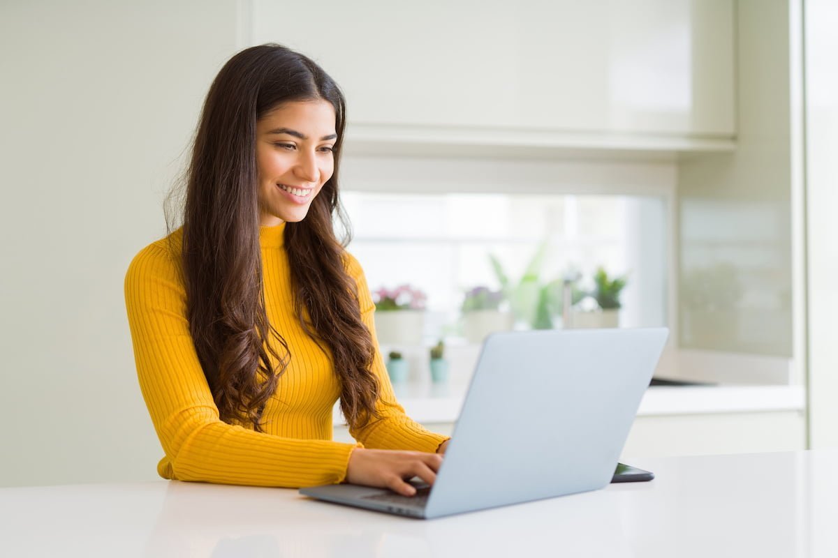 a woman smiling at her laptop as she types on it