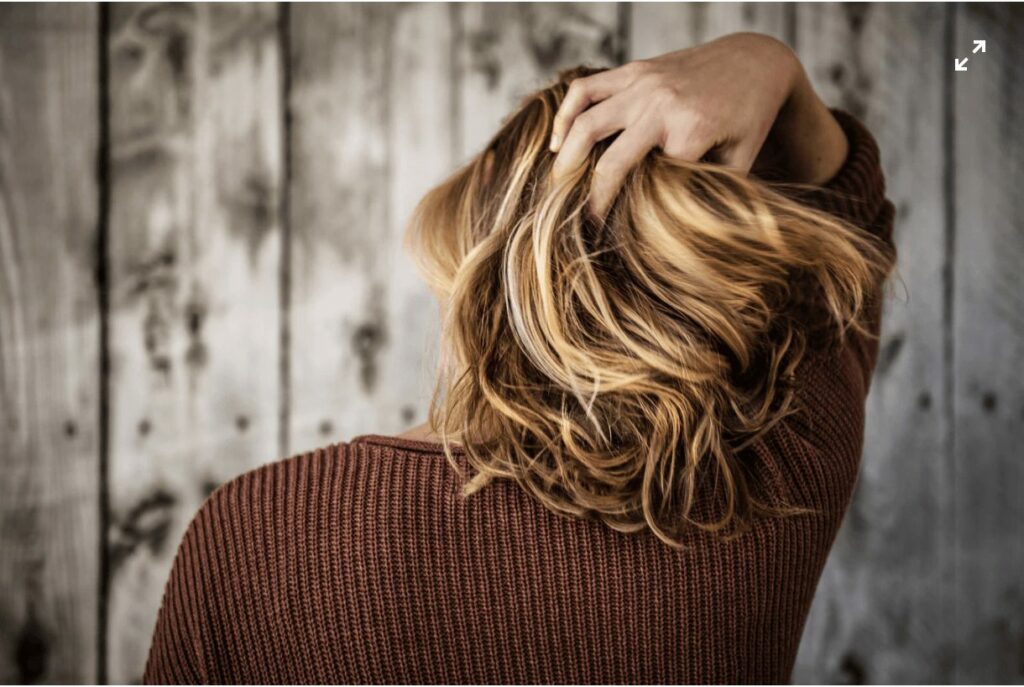 A woman combs her hand through her hair from behind