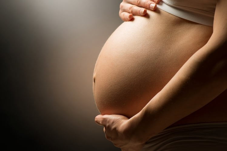 A close-up picture of a pregnant stomach being cradled by the woman’s hands