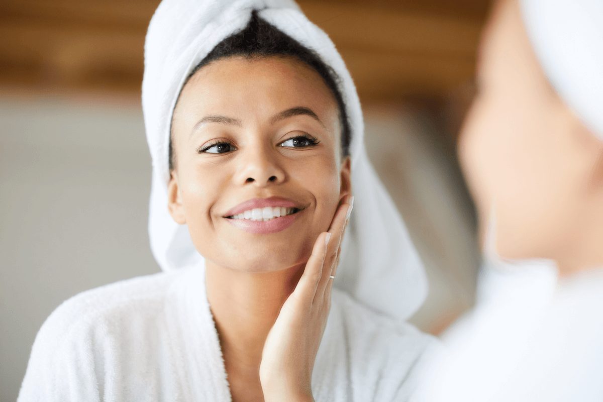 Young woman in a robe smiles and looks in the mirror