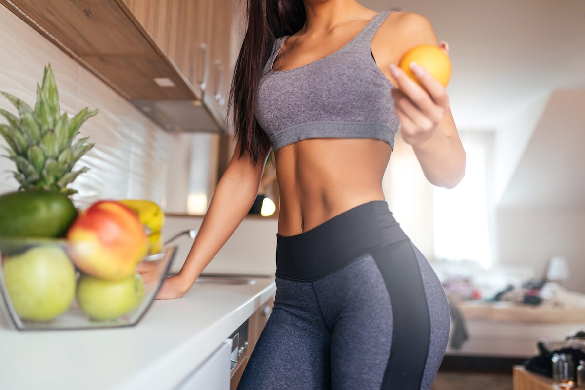 A fit woman in athletic apparel selects a piece of fruit in a kitchen