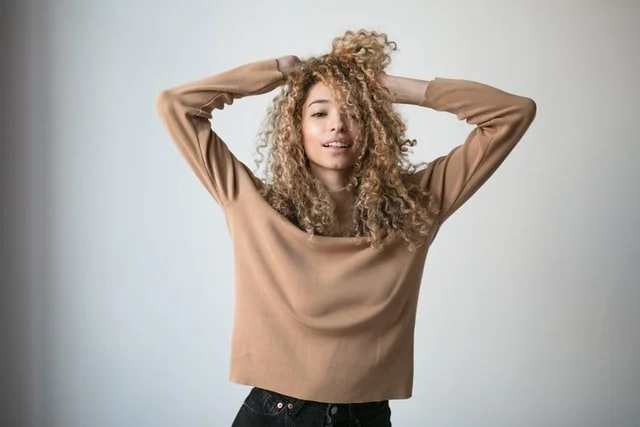 A woman with her hands in her thick, light, curly hair