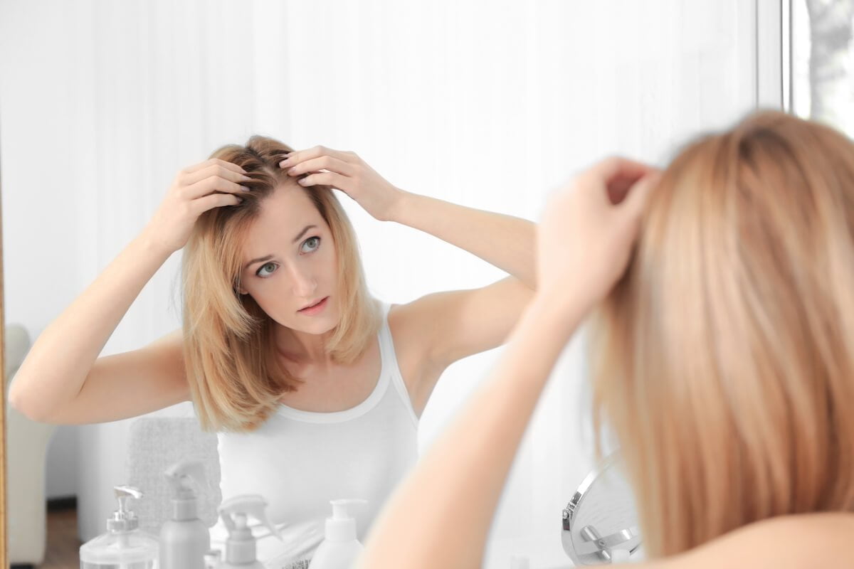 a woman parting her hair while looking in the mirror