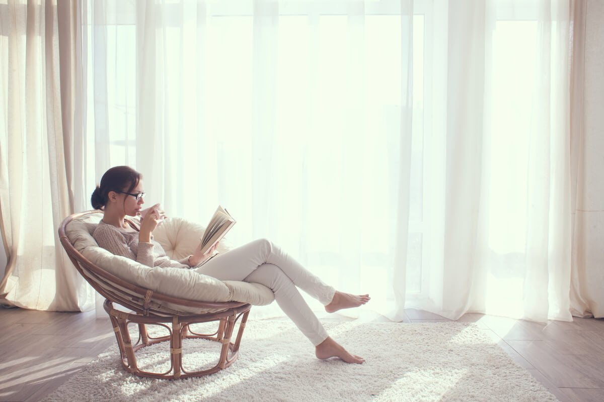 Woman in Papasan chair reading a book with a cup of tea