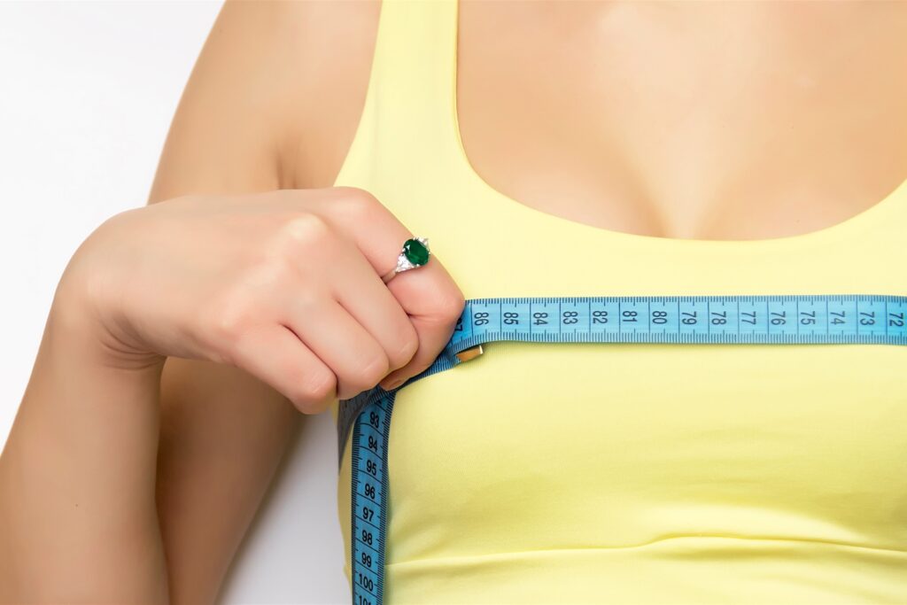A picture of a young fit happy woman checking her breast measurement over white background